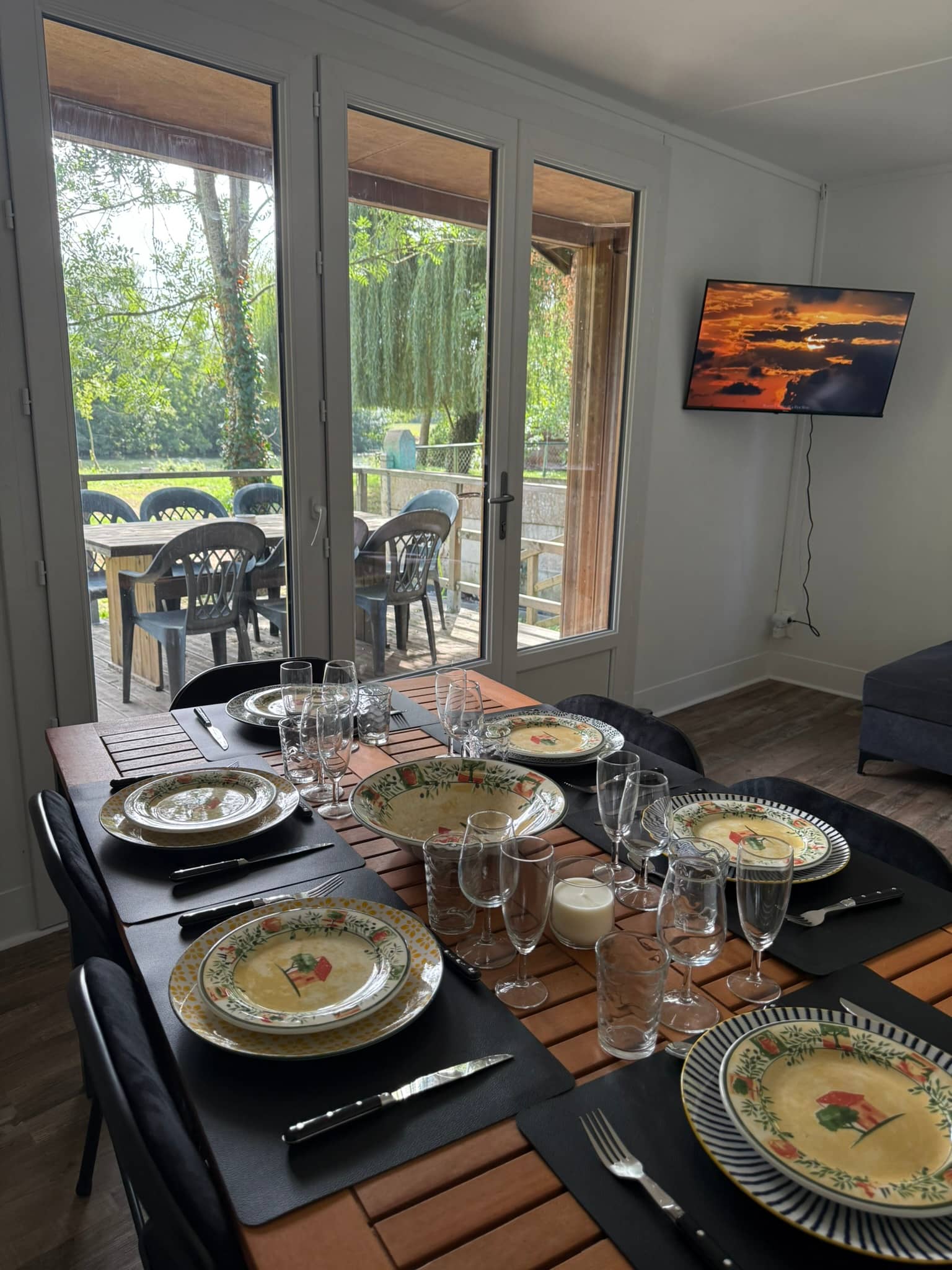Salle à manger du Chalet du Loir : la table en bois dressée pour six, portes-fenêtres grandes ouvertes sur la terrasse et le Loir